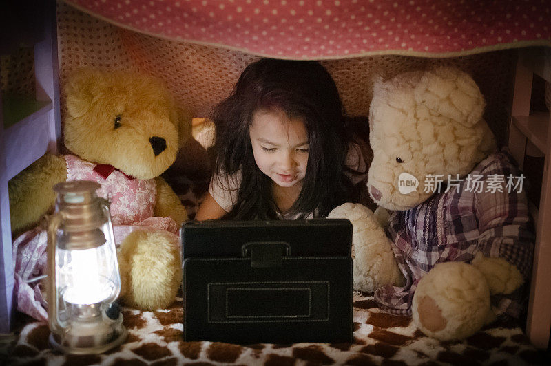 小女孩在堡垒里用iPad/平板电脑和泰迪熊玩